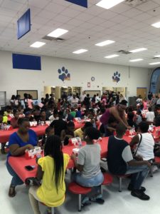 A cafeteria filled with young students and families eating KFC food